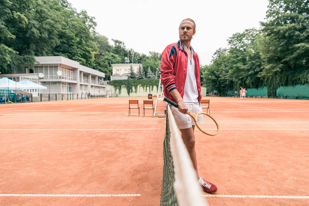 selective focus of handsome tennis player with racket standing at tennis net on court - Photo, Image