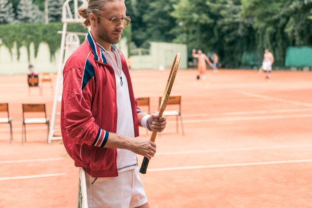 handsome old-fashioned tennis player with wooden racket standing at net on tennis court - Photo, Image