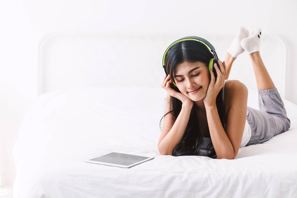 Femme écoutant de la musique avec écouteurs sur le lit
 - Photo, image