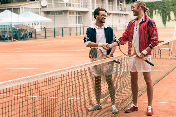 friends with wooden rackets shaking hands on tennis court with net - Photo, Image