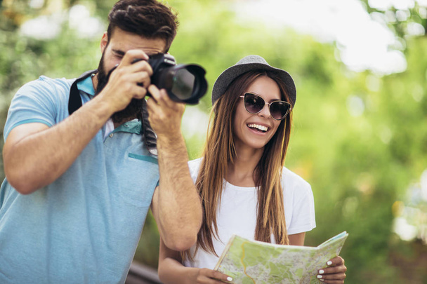 Счастливая туристическая пара делает фото с камеры и использует карту в парке в солнечный день
 - Фото, изображение
