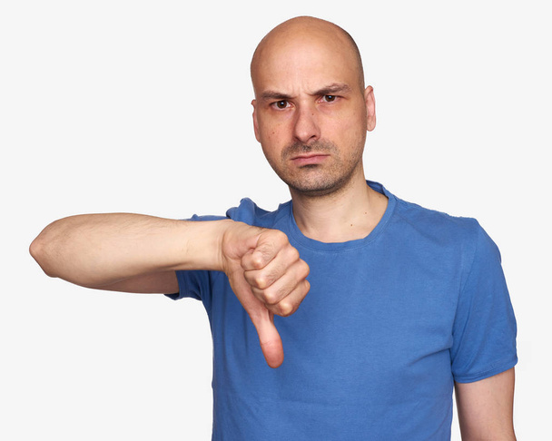 łysy mężczyzna, ubrany w niebieską koszulkę i pokazuje kciuk w dół. Na białym tle - Zdjęcie, obraz