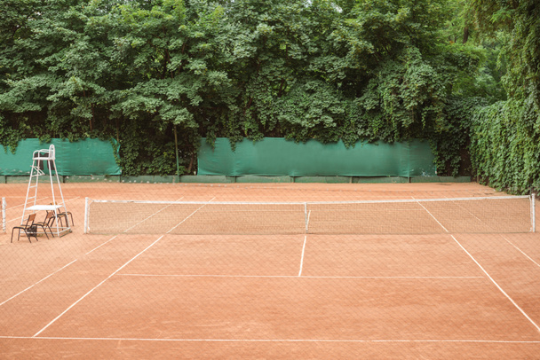 view of brown tennis court with chairs and tennis net - Фото, изображение