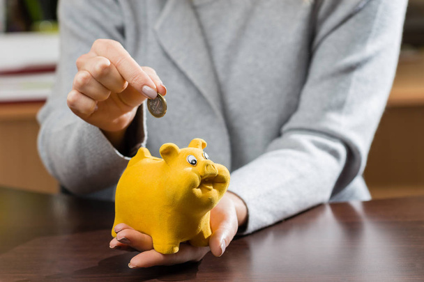 woman putting coins in a funny piggy bank. Concept of future, business, saving money, economy and investment - Photo, Image