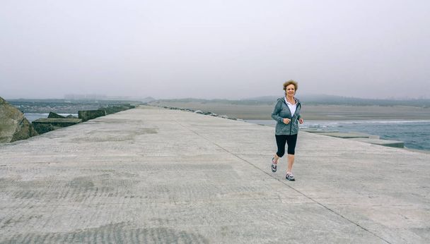 Senior sportswoman with headphones running - Photo, image
