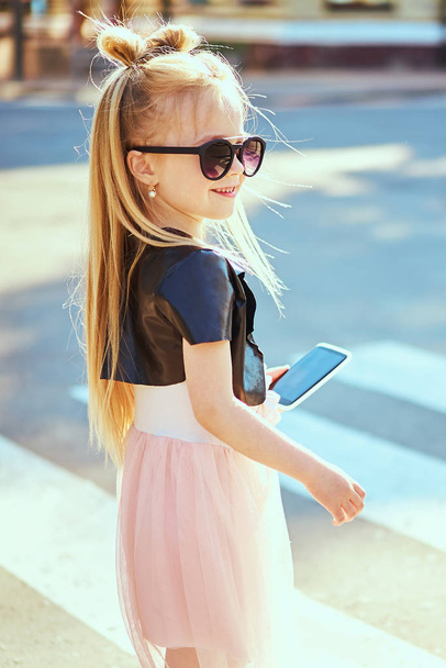 Little girl child taking picture self portrait on smartphone in city over colorful background - Photo, image