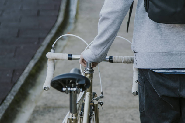 Nuori mies kävelee taaksepäin polkupyörän kanssa kaupungissa, liikenteessä ja urheilussa
 - Valokuva, kuva