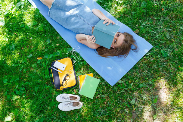 Portrait of a beautiful young caucasian woman reading a book outdoor. SLying on a grass. Top view - Foto, immagini