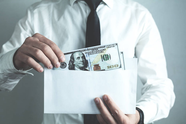 Kaukasischer Geschäftsmann steckt hundert Dollar in Umschlag. - Foto, Bild