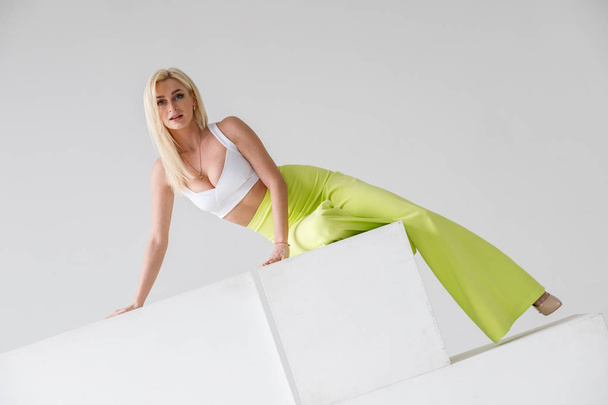 Fashion studio portrait of beauty blond model in white room interior. Shot of beauty young woman wearing green casual suit and white shirt - Φωτογραφία, εικόνα