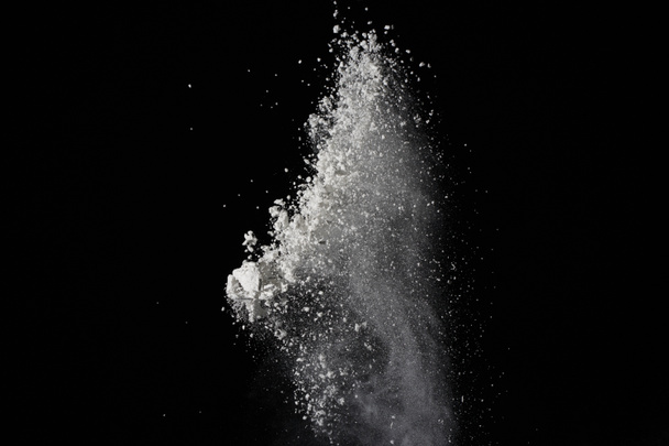Freeze motion of white dust explosion on black background. Stop motion of white powder on dark background. Explosive powder white on black background - Photo, Image