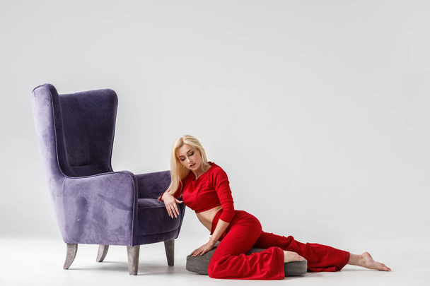 Fashion studio portrait of beauty blond model in white room interior with purple armchair. Shot of beauty young woman wearing red casual suit  - Φωτογραφία, εικόνα