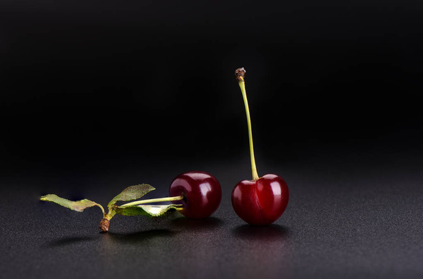 Twee rijpe zoete kersen met cherry bladeren solated op zwarte achtergrond close-up - Foto, afbeelding