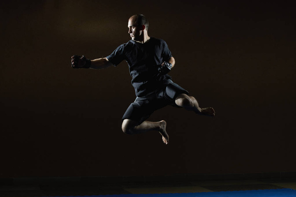 In a black T-shirt, an athlete trains a jump for a punch hand - Photo, Image