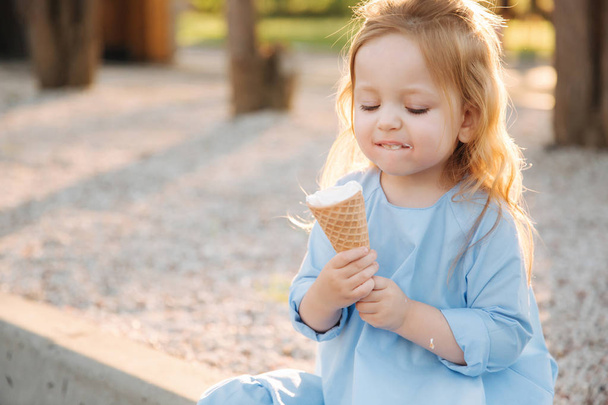 Beautiful little girl in a blue dress eating an ice cream - 写真・画像