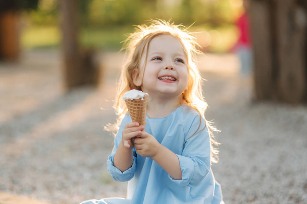 Красива маленька дівчинка в блакитній сукні їсть морозиво
 - Фото, зображення