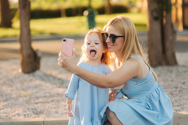 Mom and her little daughter make selfie in the park - 写真・画像
