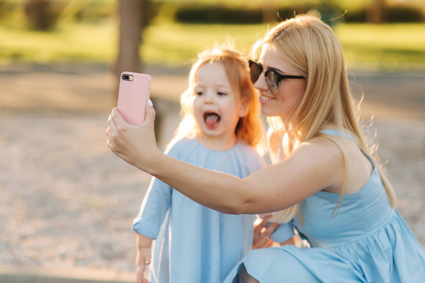 Mom and her little daughter make selfie in the park - 写真・画像