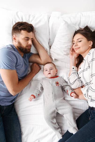 Photo of cute young family. Parents lies on bed with their little child indoors at home sleeping. - Fotoğraf, Görsel