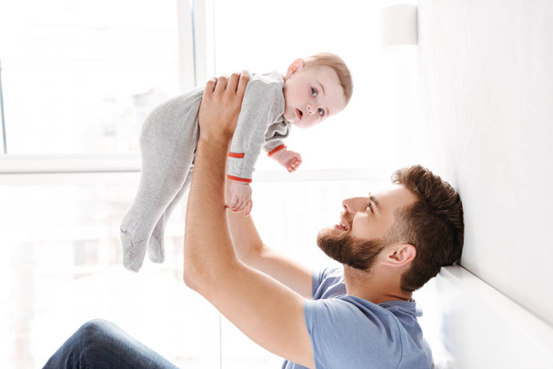 Photo of handsome happy young man father dad having fun with his little baby child son indoors at home. - Φωτογραφία, εικόνα