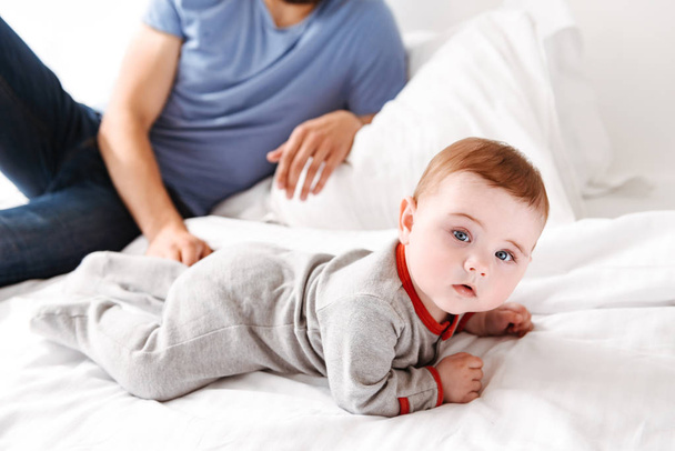 Cropped picture of young man father dad lies on bed with his little baby child son indoors at home. - Foto, Bild