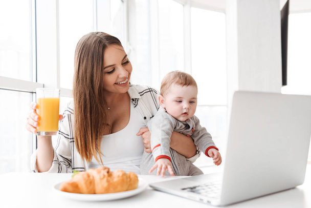 Image of happy young woman mother using laptop computer with her little child son indoors at home have a breakfast. - Valokuva, kuva