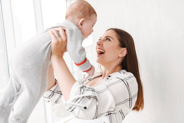 Image of happy young woman mother holding in hands her little child son indoors at home. - Valokuva, kuva