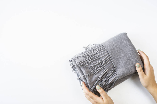 Gray cashmere female scarf folded in a rectangle with female hands on a white background. Minimalism. Top view, flat lay - Φωτογραφία, εικόνα