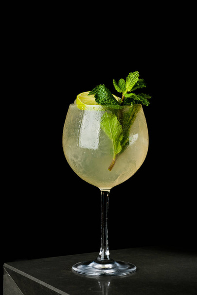 Yellow refreshing drink with lemon and mint in a glass of ice. Cocktail on a black background with bubbles and dew - Foto, immagini