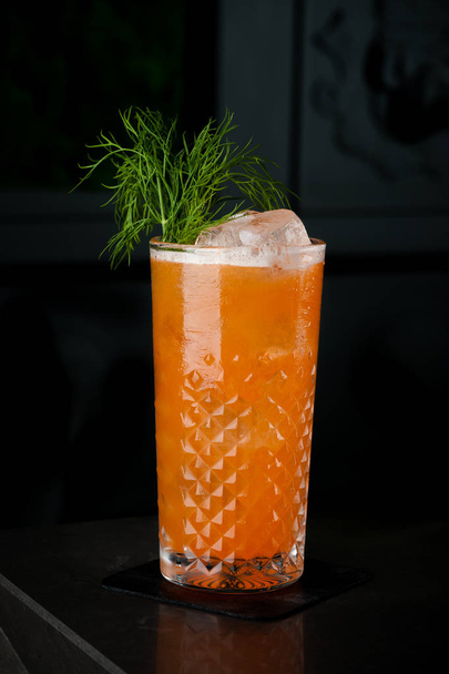 carrot cocktail with herbs in a glass of ice. Cocktail on a black background with bubbles and dew in a bright green color - Foto, imagen