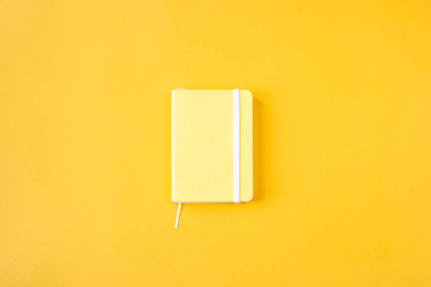 Желтый минималистичный блокнот для записей на жёлтом фоне. Планирование, ведение дневника, концепция управления временем. Вид сверху, плоский
 - Фото, изображение