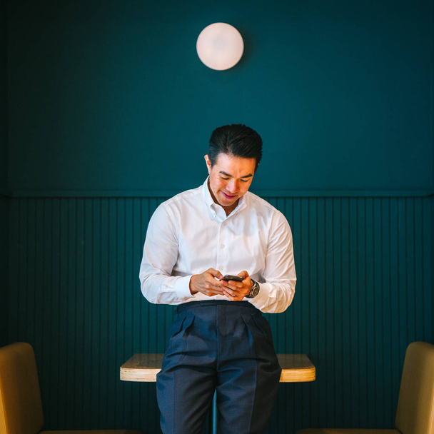 asian businessman holding smartphone standing leaning at table in modern office - Foto, Imagem