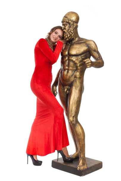 Slender beautiful girl in a red long dress is standing next to a statue on a white background. - Photo, Image