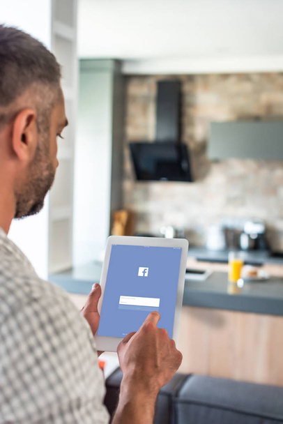 selective focus of man using digital tablet with facebook logo on screen in kitchen  - Foto, Bild