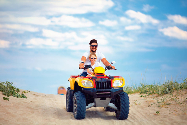 happy family, father and son riding on atv quad bike at sandy beach - Photo, image