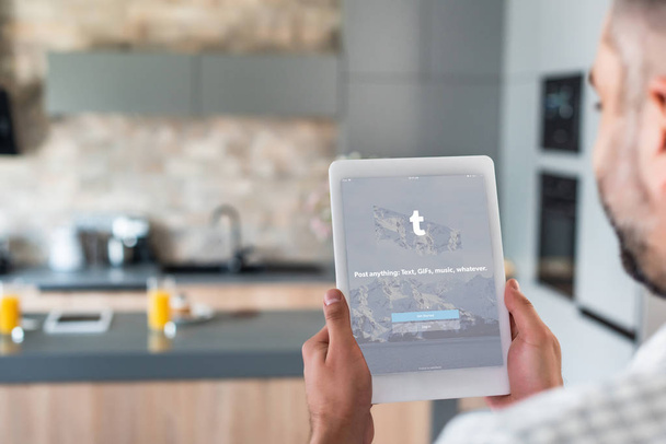 Selective focus of man using digital tablet with tumblr logo on screen in kitchen - Фото, зображення