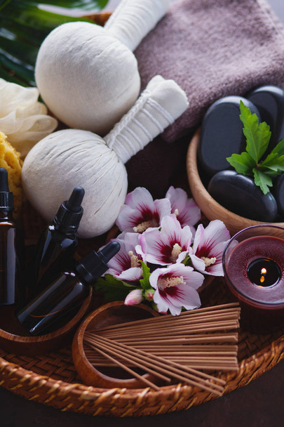 bolas de compresa de hierbas con guijarros de spa y flores de hibisco con botellas de aceite de aromaterapia en bandeja de mimbre
  - Foto, Imagen