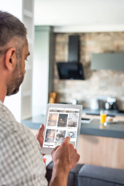 selective focus of man using digital tablet with pinterest website on screen in kitchen  - Foto, Bild