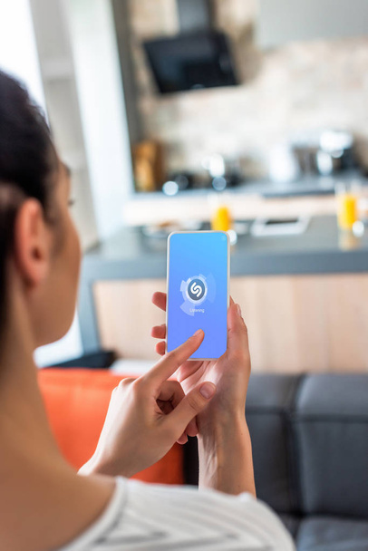 selective focus of woman using smartphone with shazam logo in kitchen - Фото, зображення
