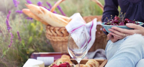 Léto - dívka na pikniku na louce. Sýr brie, bageta, jahody, třešně, víno, croissanty a baske - Fotografie, Obrázek