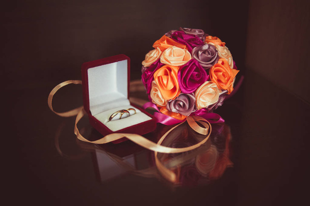 Anéis de casamento em uma caixa com um buquê em uma superfície escura com reflexão
 - Foto, Imagem
