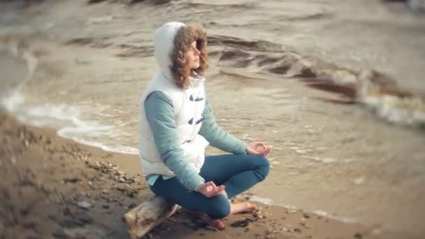 Mujer sentada en una pose de loto yoga sobre la arena cerca del agua
 - Metraje, vídeo