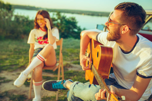 Couple sitting and resting on the beach playing guitar on a summer day near river - Foto, Bild