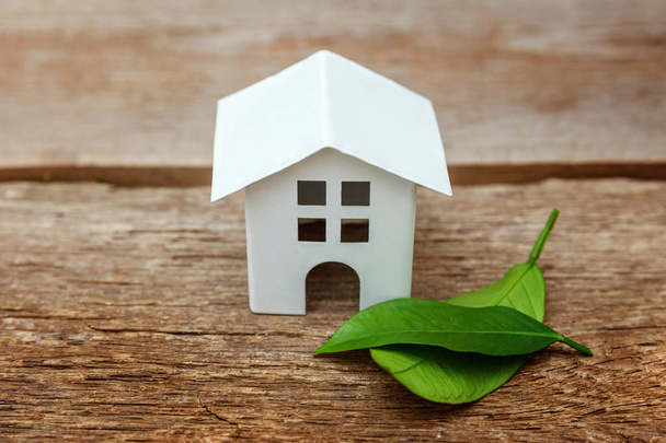 Miniature white toy model house with green leaves on wooden backgdrop. Eco Village, abstract environmental background. Real estate mortgage property insurance dream home ecology concept - Photo, Image