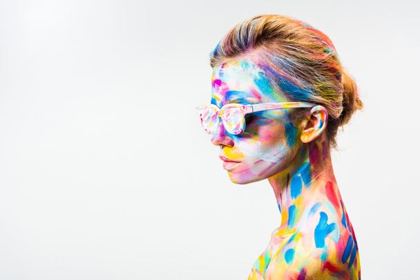 boční pohled atraktivní dívka s barevnými světlé bodyart a sluneční brýle, izolované na bílém - Fotografie, Obrázek
