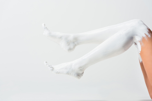cropped image of girl with legs painted with white paint lying on floor isolated on white - Foto, Imagem