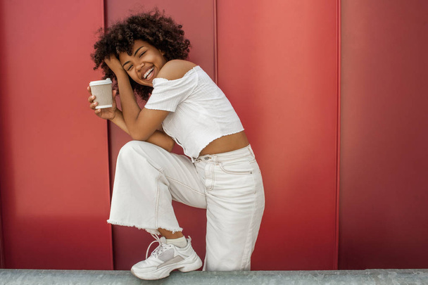 boldog afro-amerikai lány gazdaság eldobható kávéscsésze, és nevetve utcában - Fotó, kép