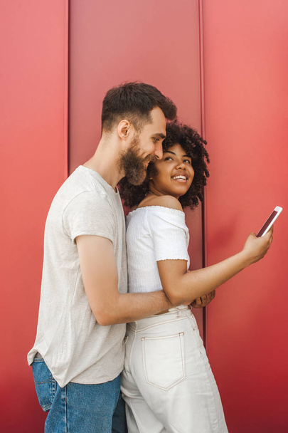 handsome young man hugging smiling girlfriend using smartphone on street - Fotó, kép