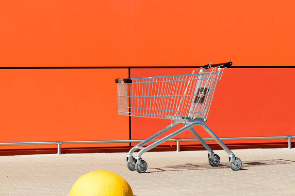 metal empty shopping cart near the orange wall of the shopping c - Foto, Bild