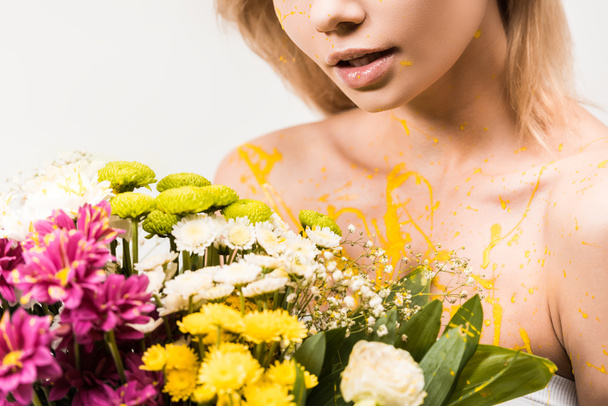 cropped image of woman with yellow paint on body holding bouquet of flowers isolated on white - Photo, Image